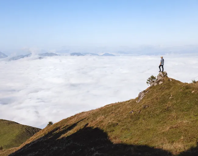 Person, die auf einem Felsen in den Tiroler Bergen steht, über einer Wolkendecke.